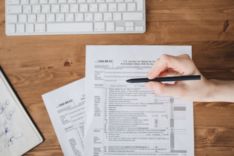 台馬跨境稅務 — Close-up of a hand holding a pen over US tax forms on a wood
